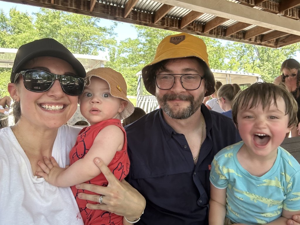 The KC Pancake Co. family: mom, dad and their two young boys smiling together under a park shelter